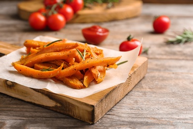 Board with sweet potato fries on wooden table, closeup. Space for text