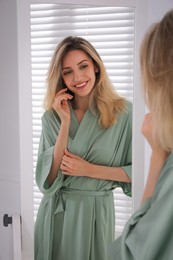 Photo of Pretty young woman in beautiful silk robe near mirror at home