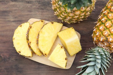 Photo of Cut and whole ripe pineapples on wooden table, flat lay