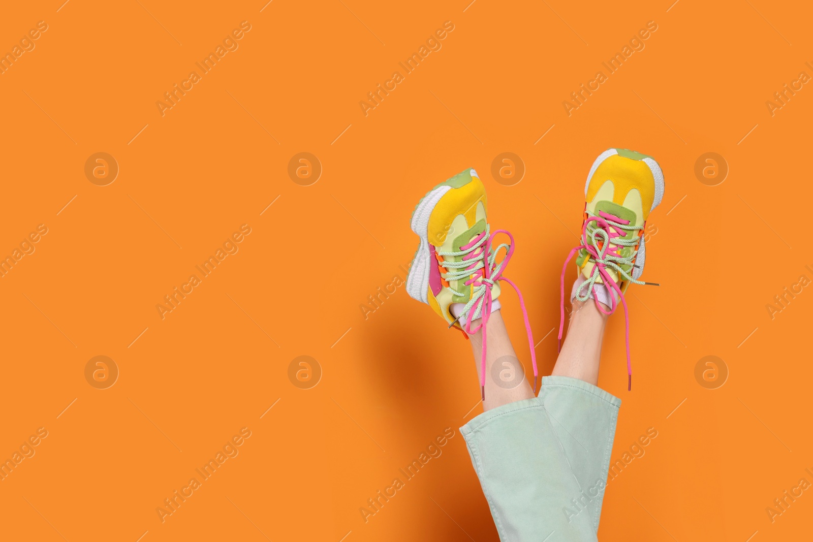 Photo of Woman wearing pair of new stylish sneakers on orange background, closeup. Space for text
