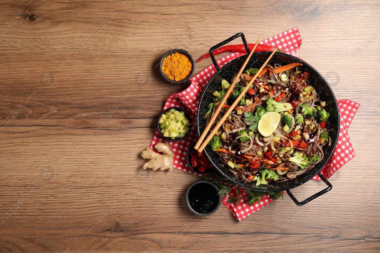 Photo of Stir-fry. Tasty noodles with meat in wok, chopsticks and ingredients on wooden table, flat lay. Space for text