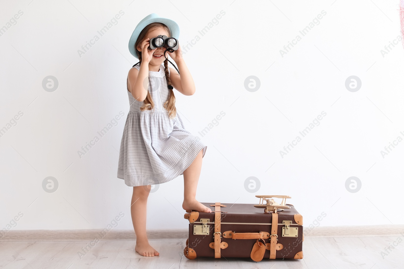 Photo of Adorable little child playing traveler with suitcase indoors