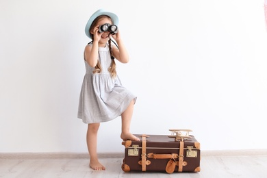 Adorable little child playing traveler with suitcase indoors