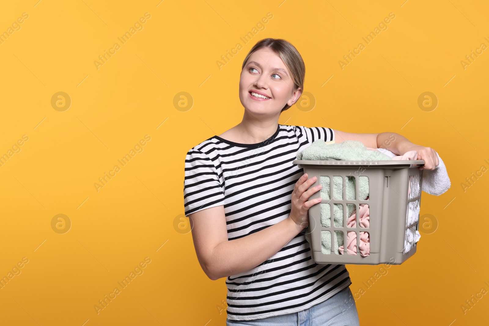 Photo of Happy woman with basket full of laundry on orange background. Space for text