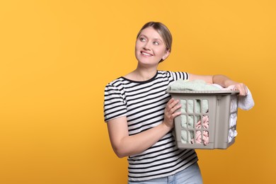 Happy woman with basket full of laundry on orange background. Space for text