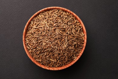Photo of Wooden bowl with cumin seeds on dark background, top view