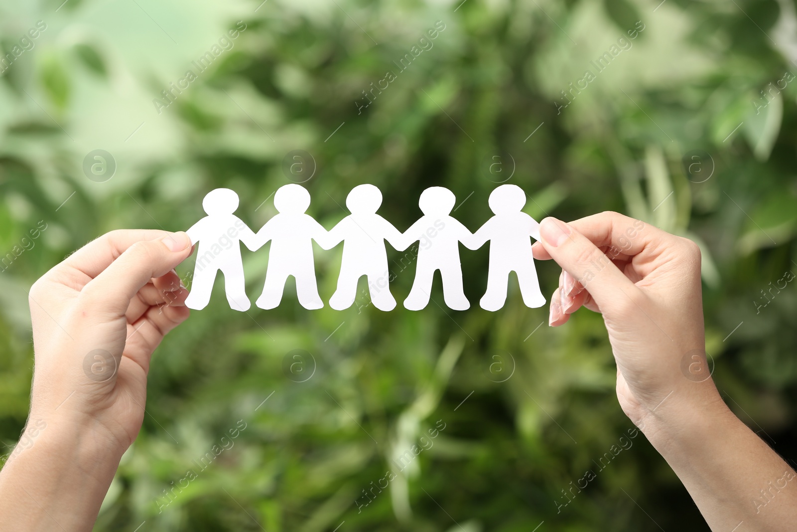 Photo of Woman holding paper people chain on blurred green background, closeup. Unity concept