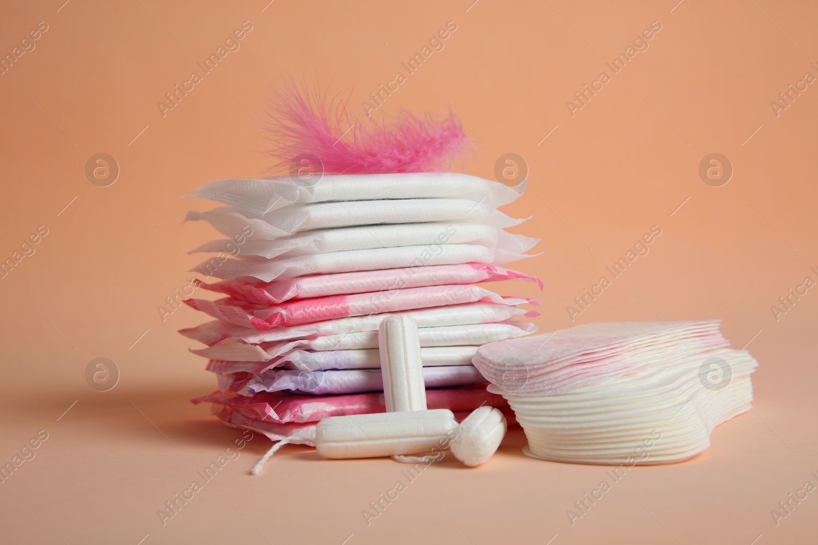 Photo of Menstrual pads with pink feather and other period products on pale orange background