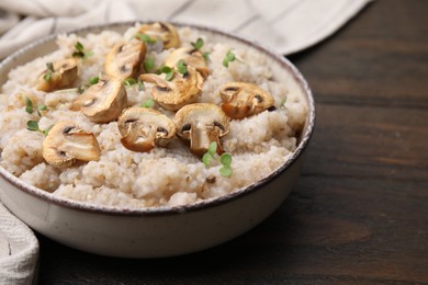 Photo of Delicious barley porridge with mushrooms and microgreens in bowl on wooden table, closeup