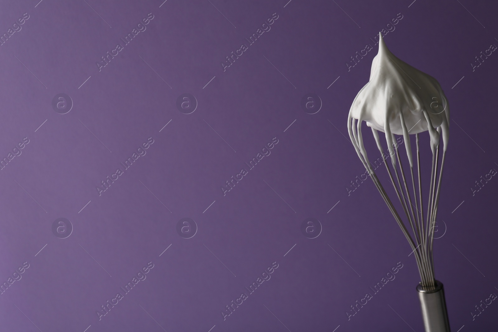 Photo of Whisk with whipped cream on violet background. Space for text