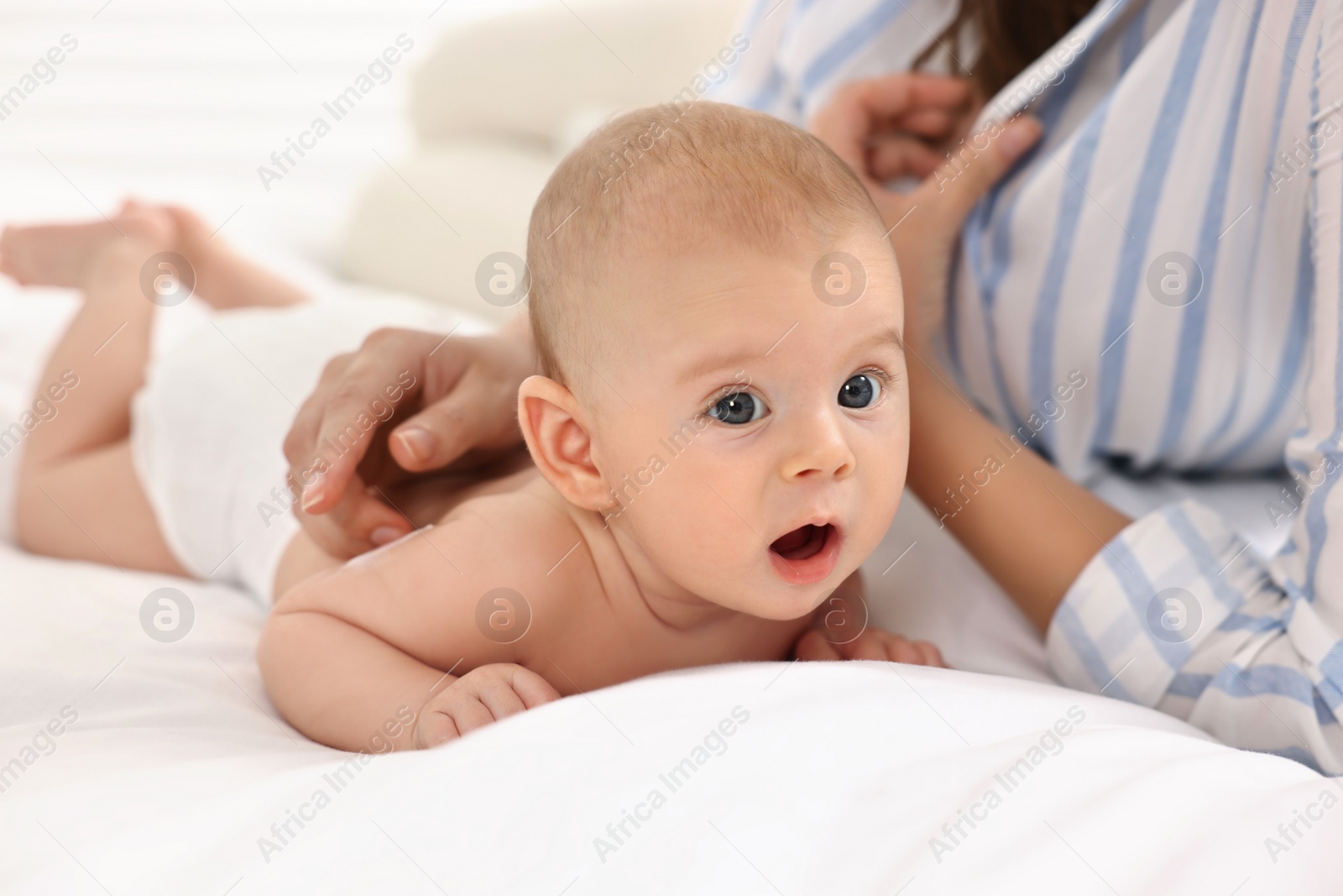 Photo of Woman applying body cream onto baby`s skin on bed, closeup