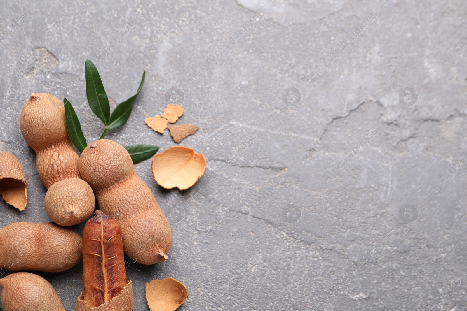 Photo of Ripe tamarinds and fresh leaves on grey table, flat lay. Space for text