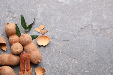 Ripe tamarinds and fresh leaves on grey table, flat lay. Space for text