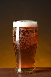 Photo of Glass with fresh beer on wooden table against dark background