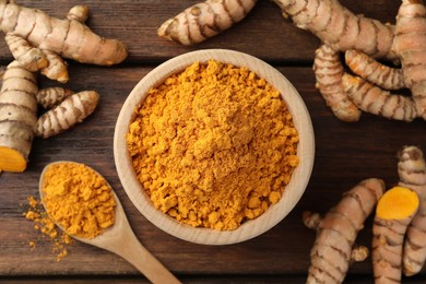 Photo of Aromatic turmeric powder and raw roots on wooden table, flat lay