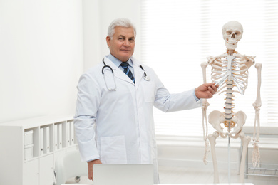 Photo of Senior orthopedist with human skeleton model in clinic