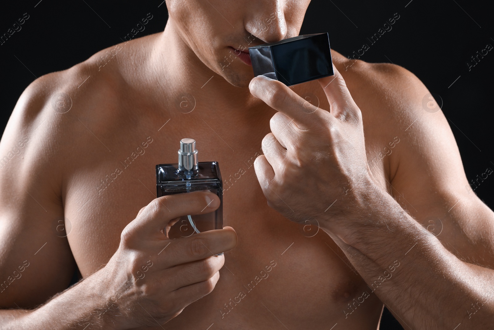 Photo of Young man smelling perfume on black background, closeup