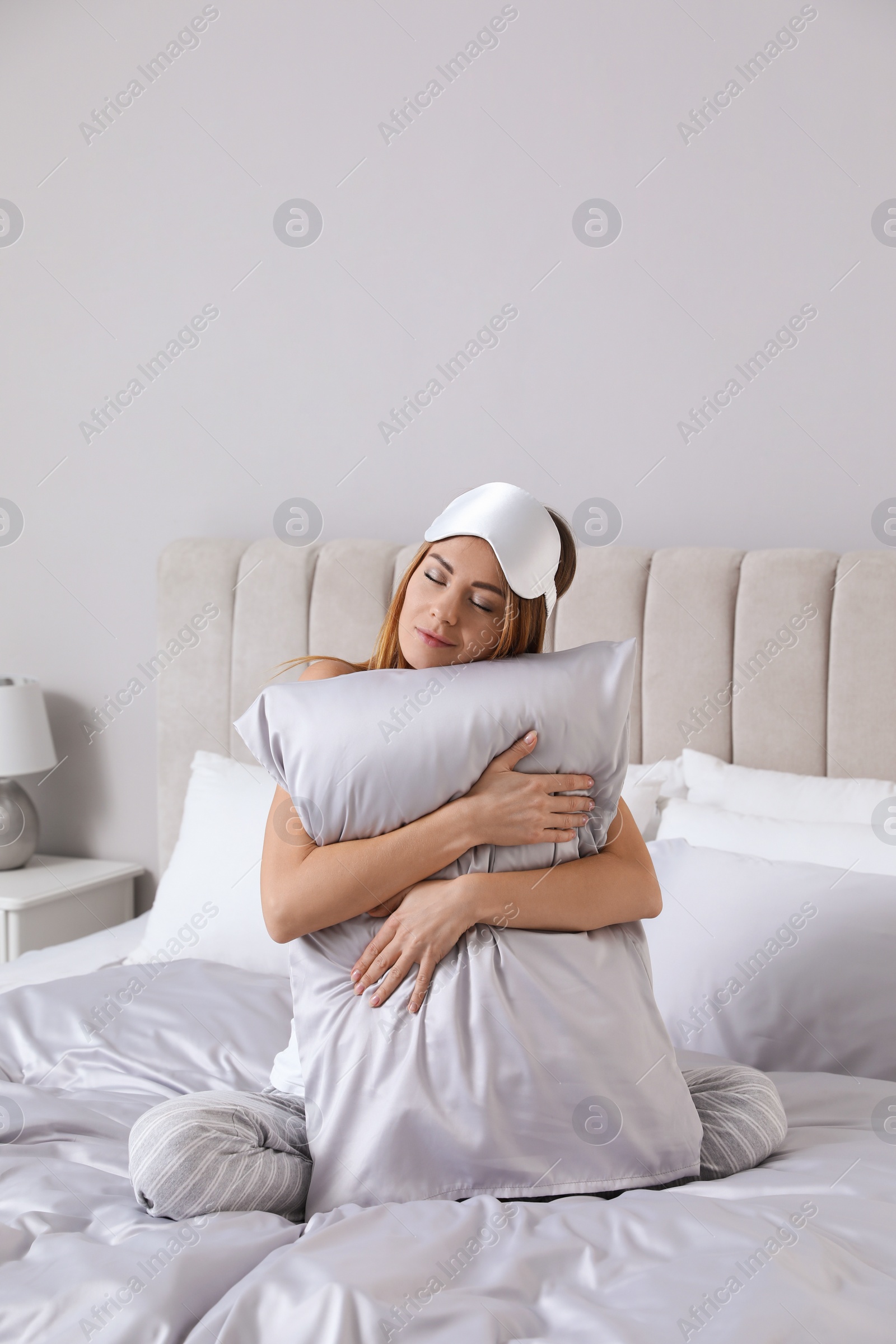 Photo of Beautiful woman hugging pillow on comfortable bed with silky linens