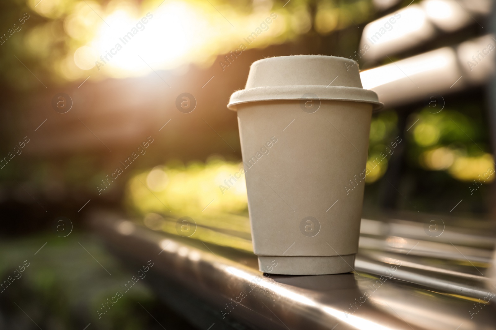 Photo of Cardboard takeaway coffee cup with lid on wooden bench outdoors, space for text