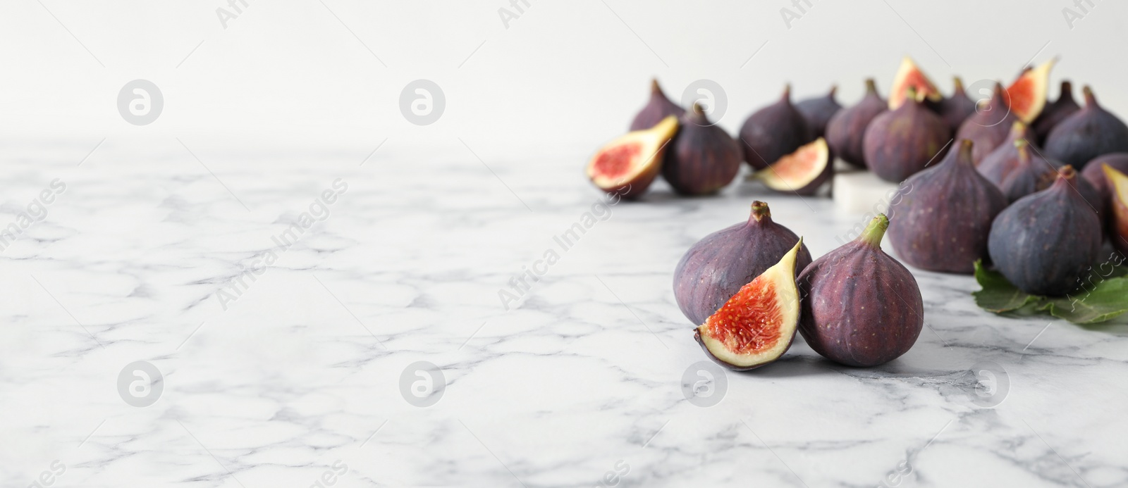 Photo of Whole and cut tasty fresh figs on white marble table. Space for text