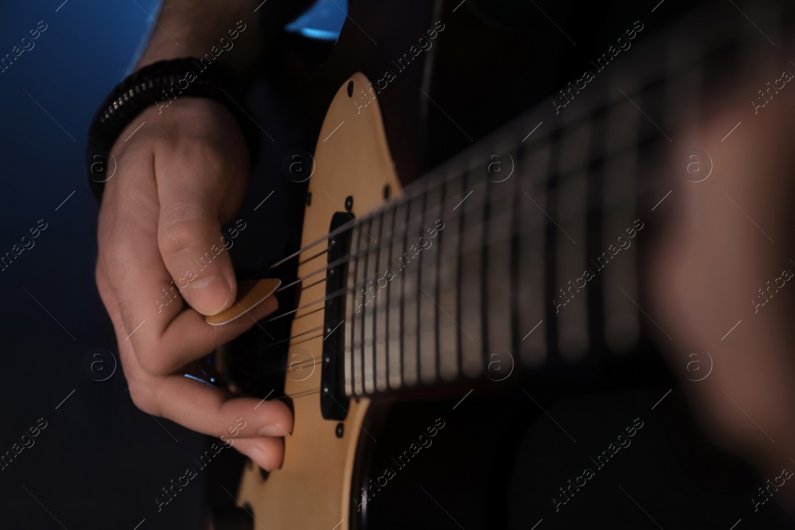 Photo of Man playing electric guitar on dark background, closeup. Rock music