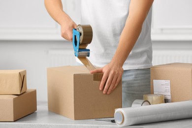 Photo of Man packing box with adhesive tape indoors, closeup