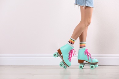 Photo of Young woman with retro roller skates near white wall, closeup. Space for text