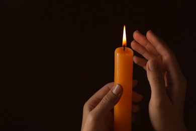 Woman holding burning church candle on black background, closeup. Space for text