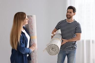 Photo of Smiling couple holding rolled carpets in room