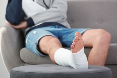 Young man with broken leg in cast sitting on sofa at home