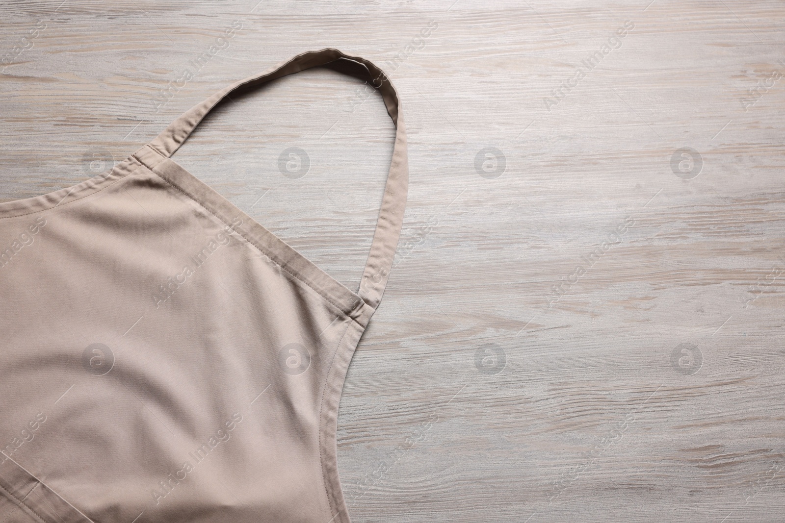 Photo of Stylish beige apron on light wooden table, top view. Mockup for design