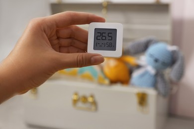 Photo of Woman holding digital hygrometer with thermometer on blurred background, closeup