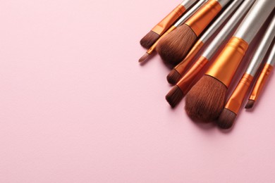 Photo of Set of makeup brushes on pink background, above view. Space for text