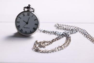 Photo of Silver pocket clock with chain on white wooden table, closeup