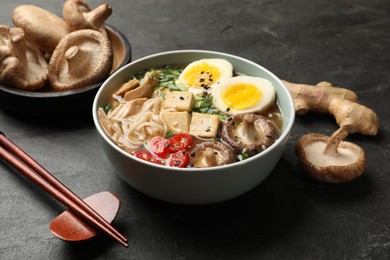 Photo of Noodle soup. Bowl of delicious ramen, ingredients and chopsticks on black table, closeup