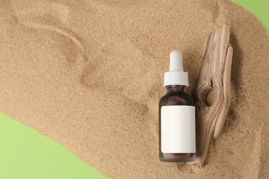 Bottle with serum and bark on sand against green background, top view. Cosmetic product