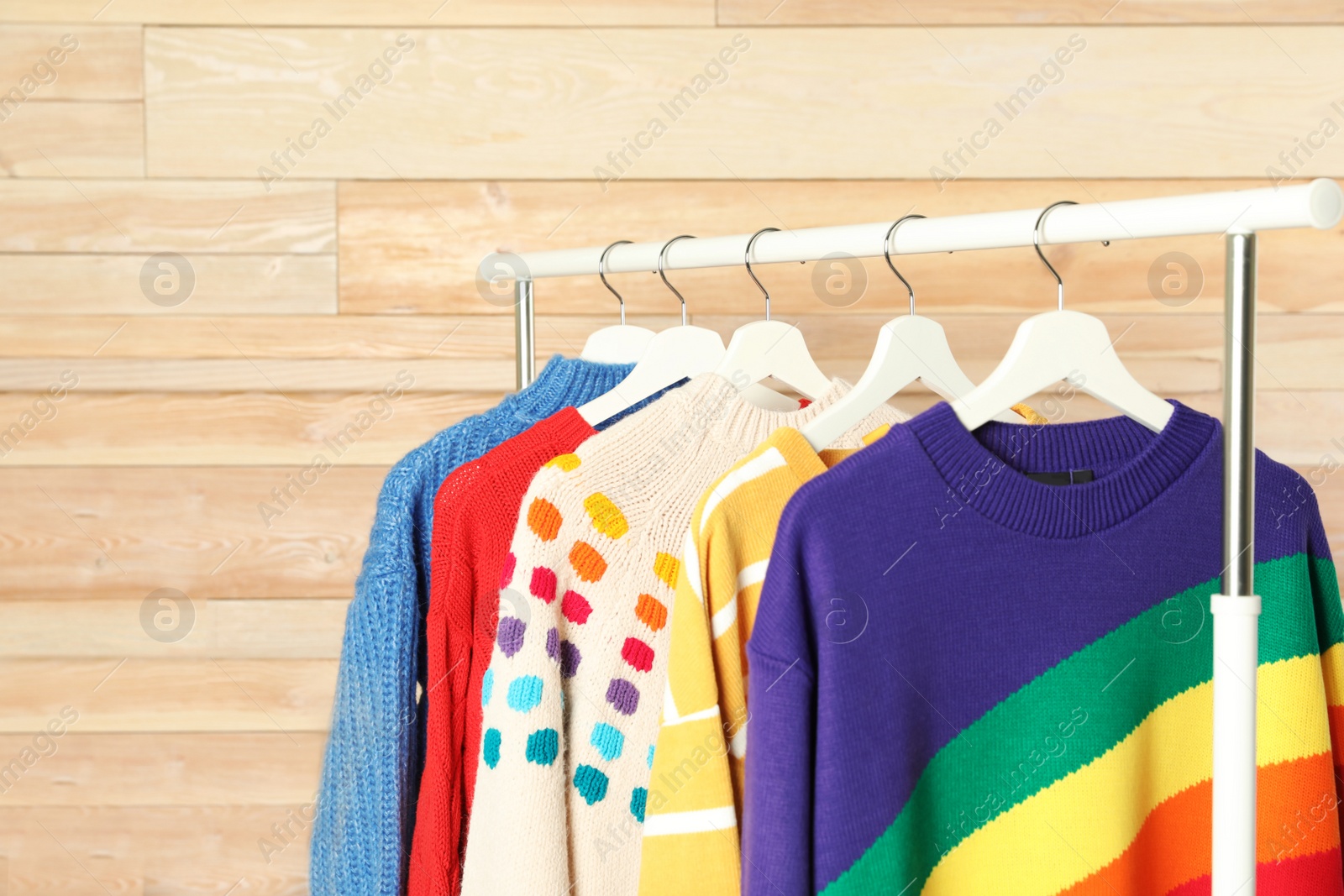 Photo of Collection of warm sweaters hanging on rack against wooden wall