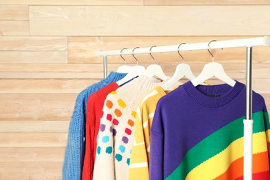 Collection of warm sweaters hanging on rack against wooden wall