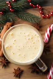 Photo of Glass of delicious eggnog, candy cane and anise stars on wooden table, flat lay