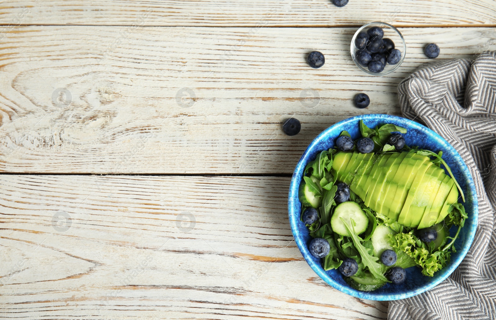 Photo of Delicious avocado salad with blueberries in bowl on white wooden table, flat lay. Space for text