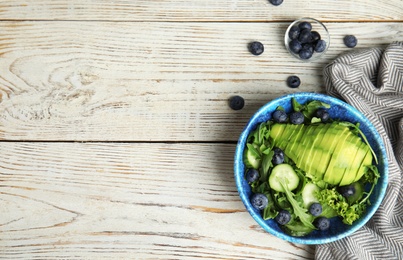 Delicious avocado salad with blueberries in bowl on white wooden table, flat lay. Space for text