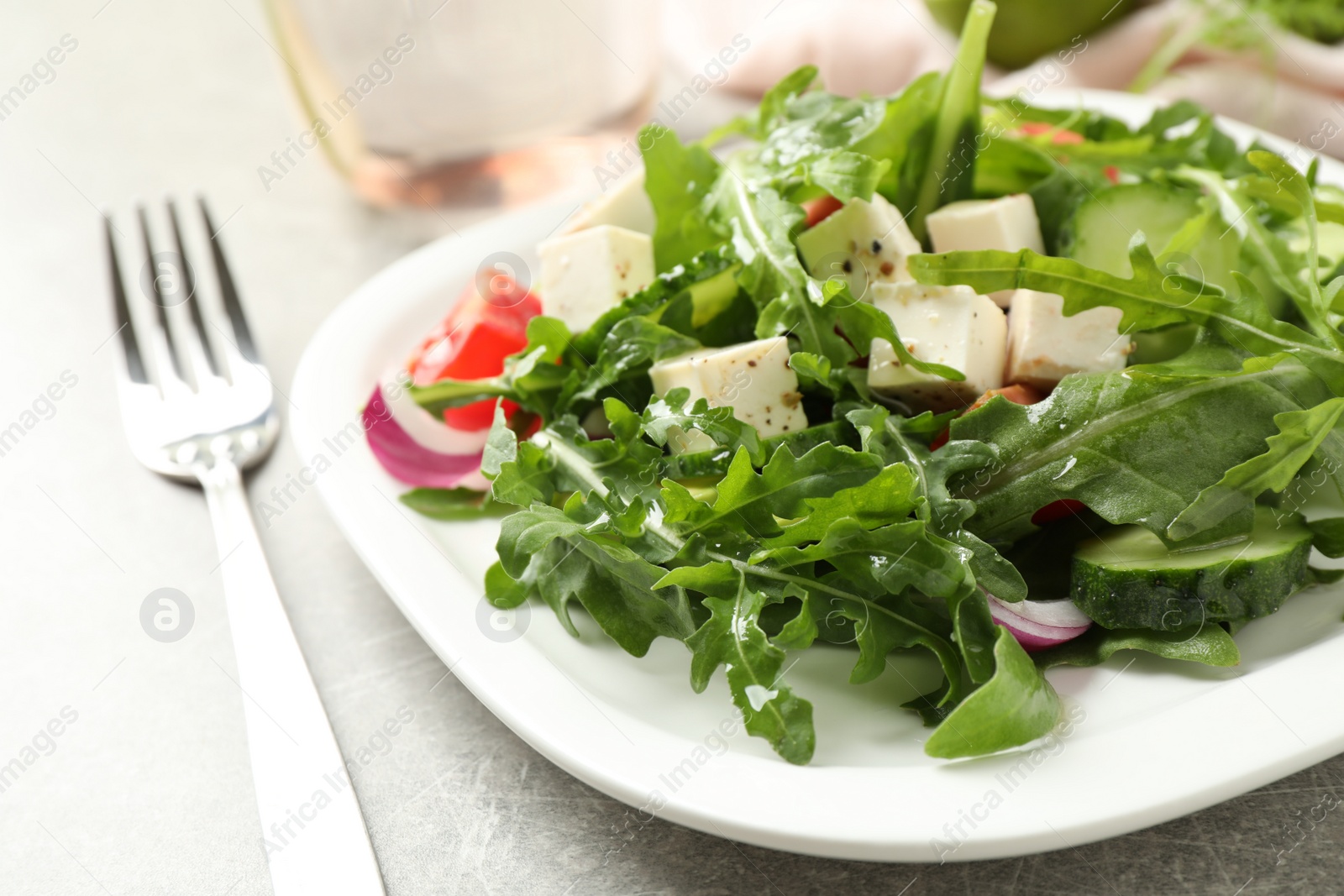 Photo of Delicious salad with feta cheese, arugula and vegetables on grey table, closeup