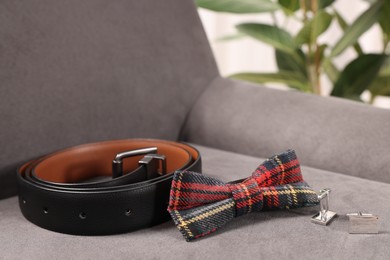 Stylish tartan bow tie, belt and cufflinks on grey armchair, closeup