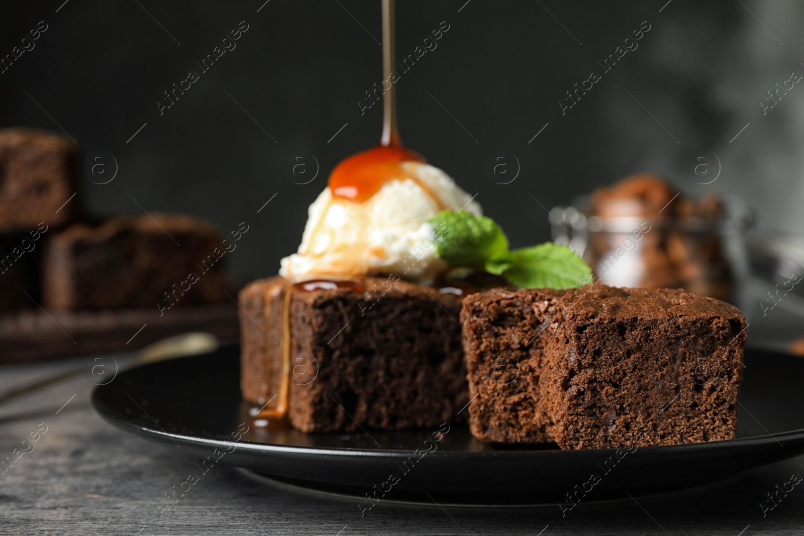 Photo of Pouring sauce onto ice-cream with fresh brownies on plate. Delicious chocolate pie