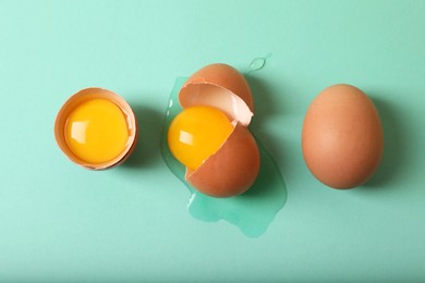 Photo of Cracked and whole chicken eggs on turquoise background, flat lay