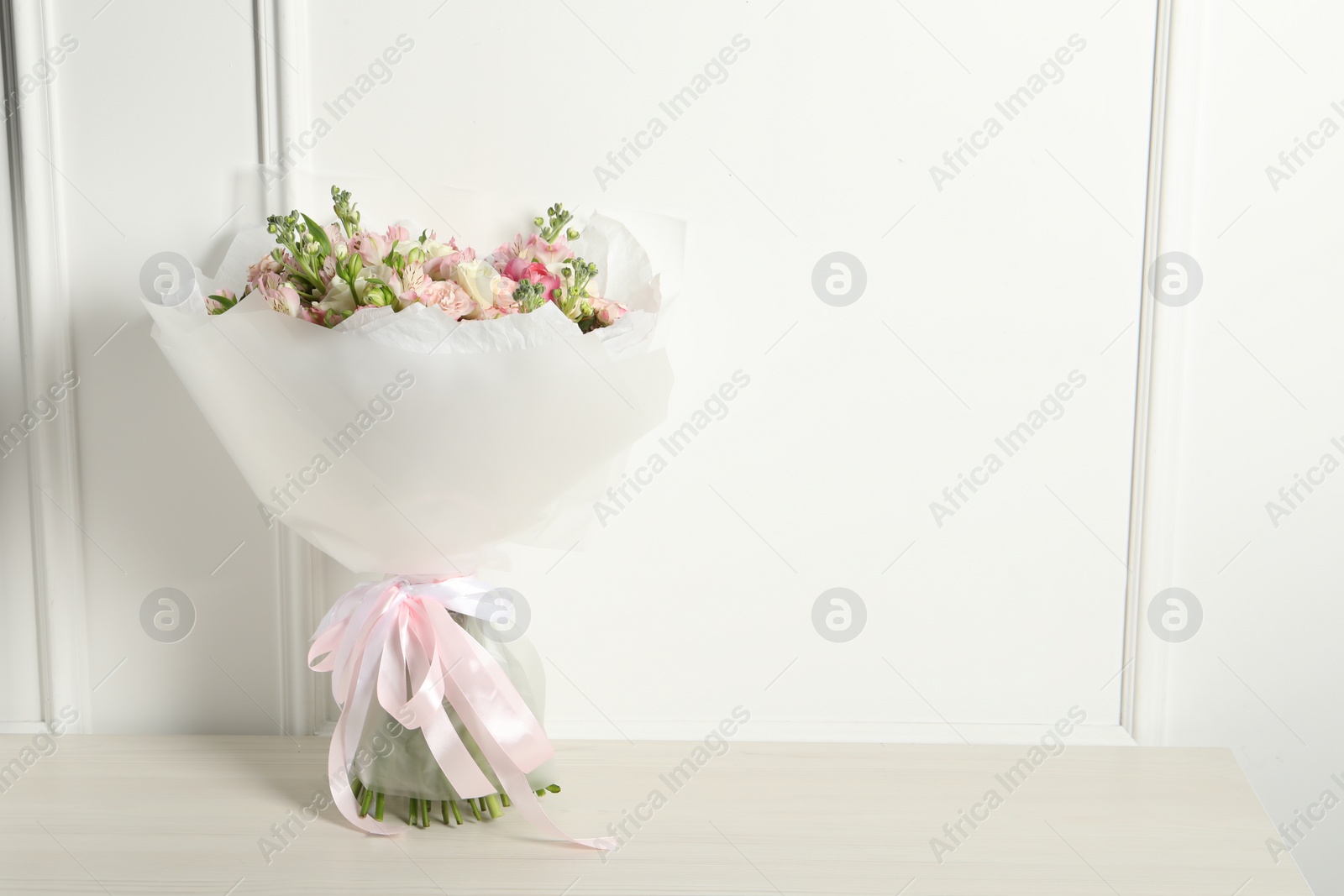 Photo of Beautiful bouquet of fresh flowers on wooden table near white wall, space for text