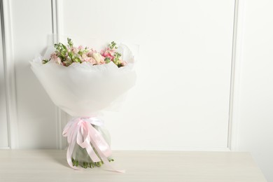 Beautiful bouquet of fresh flowers on wooden table near white wall, space for text