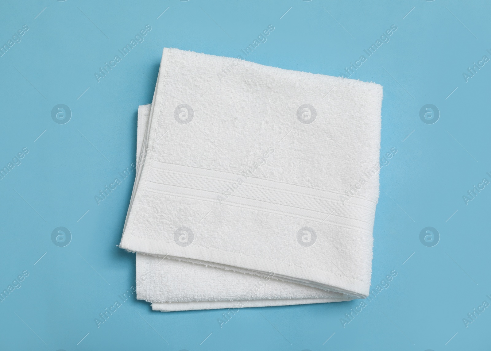 Photo of Folded white beach towel on light blue background, top view