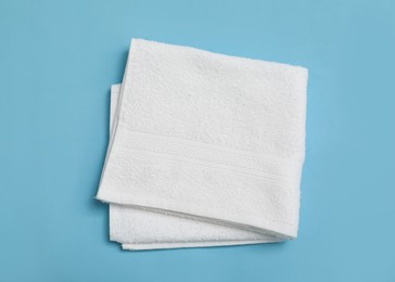 Folded white beach towel on light blue background, top view