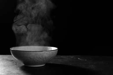 Photo of Bowl with white steam on black slate table. Space for text